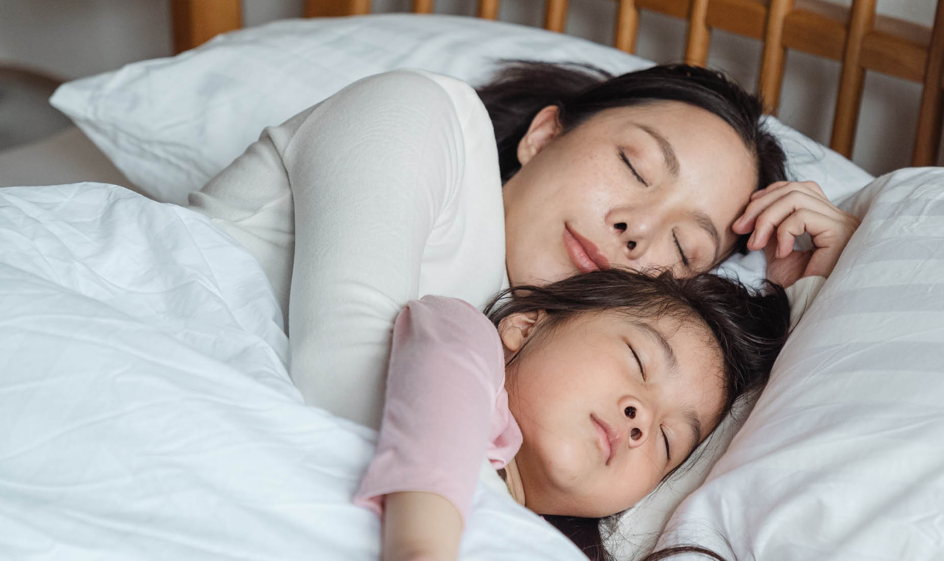 A mother and daughter of East Asian descent cuddling in bed looking contented.